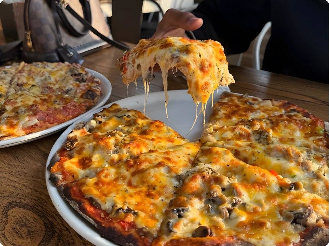 A cheesy slice of pizza lifted from a wood-fired pizza at Omateko restaurant